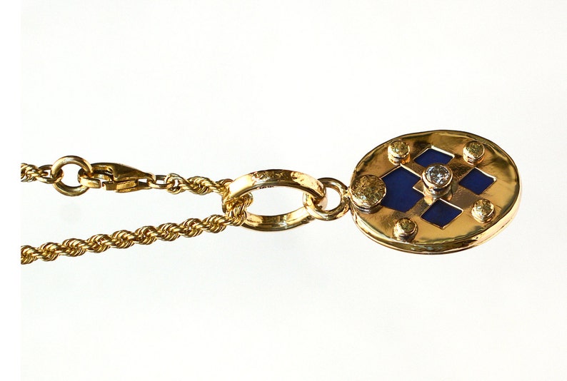 May include: A gold necklace with a pendant featuring a blue and gold geometric design with a small diamond in the center.