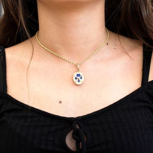 May include: A gold chain necklace with a blue and gold pendant. The pendant is oval shaped and has a geometric design.