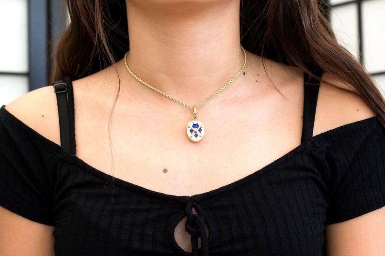 May include: A gold chain necklace with a blue and gold pendant. The pendant is oval shaped and has a geometric design.