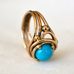 May include: A gold ring with a turquoise stone set in a delicate, intricate design. The ring features multiple bands and small gold accents.