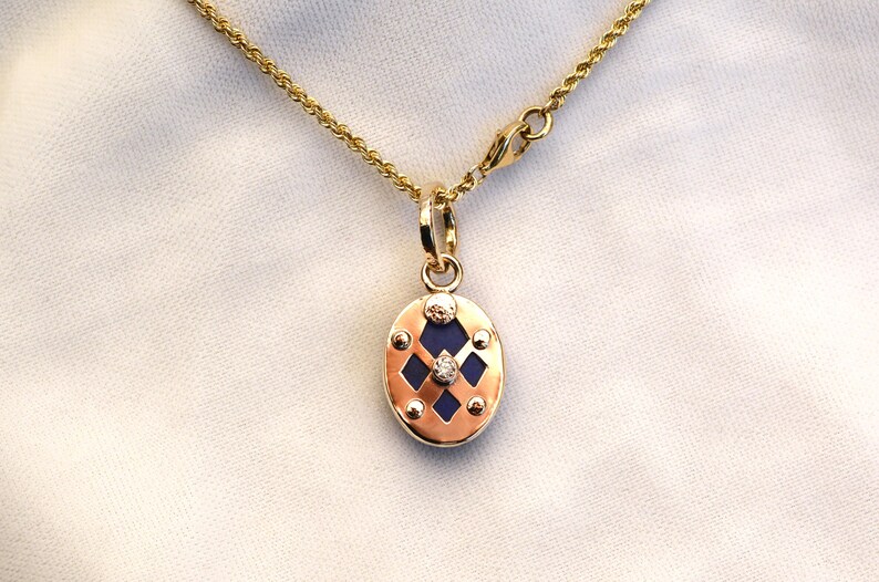 May include: A gold chain necklace with a pendant featuring a blue oval stone surrounded by a gold frame with a diamond in the center.