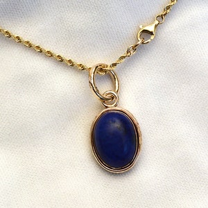 May include: A gold chain necklace with a pendant featuring a dark blue oval gemstone.