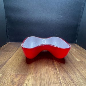 May include: A bright red, organically shaped bowl with a white interior. The bowl has a glossy finish and a unique, flowing design. This decorative piece could be used for serving or as a decorative accent.
