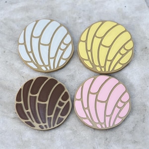 May include: Four colorful, round concha-shaped items. Each has a tan base with a patterned top in white, yellow, brown, and pink. The conchas are arranged in a square, with each one facing the viewer.