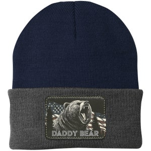 May include: A navy blue and gray beanie with a patch featuring a roaring bear in front of an American flag and the text "Daddy Bear".