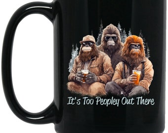 May include: Black coffee mug with a graphic of three cartoon Bigfoot characters holding beers and the text "It's Too Peopley Out There".