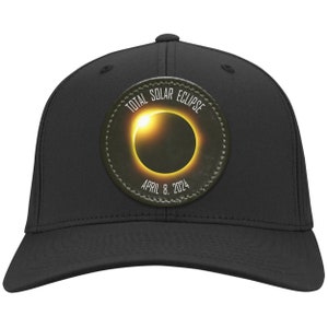 May include: Black baseball cap with a circular patch featuring a graphic of a total solar eclipse with the text "TOTAL SOLAR ECLIPSE APRIL 8, 2024".
