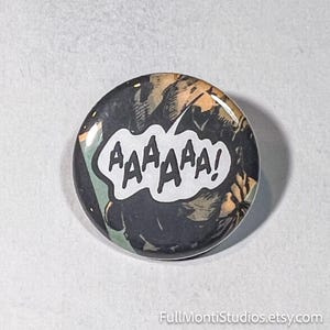 May include: Round button with a comic book style design. The button features a speech bubble with the word "AAAAAA!" in white letters against a black and tan background. The button has a glossy finish.