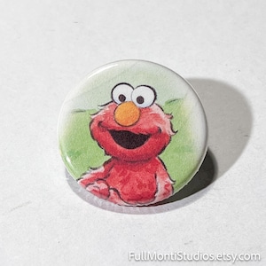 May include: A round button featuring a watercolor illustration of Elmo from Sesame Street. Elmo is red with a large orange nose, big eyes, and a wide smile. The background is light green. The text "FullMontiStudios.etsy.com" is at the bottom.