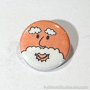 May include: A round button with a cartoon illustration of a face. The face has an orange background, white clouds for eyebrows, black eyes, a black nose, and a white beard with a smiling mouth. The button is glossy.