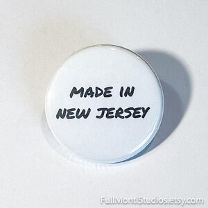 May include: A white round button with the text "MADE IN NEW JERSEY" in black, handwritten-style font. The button is centered in the image, casting a shadow on a white background. The Etsy shop name is visible at the bottom.