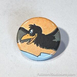 May include: Round button featuring a cartoon crow in flight against an orange and blue background. The crow is black with a yellow beak and blue eyes. The button has a glossy finish and the text "FullMontiStudios.etsy.com" at the bottom.