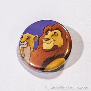 May include: A round button featuring a colorful illustration of two lions against a blue background. The lions are depicted in a cartoon style with shades of yellow, brown, and tan. The button has a glossy finish and the text "FullMontiStudios.etsy.com" is visible.