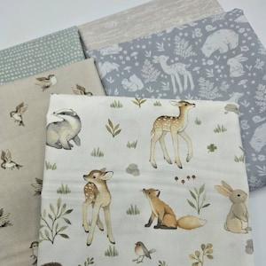 May include: A collection of four folded fabric squares featuring woodland themes. The top piece displays a white background with illustrations of a fawn, fox, rabbit, hedgehog, and birds. Other pieces include grey with white animals, beige with birds, and light green with dots.
