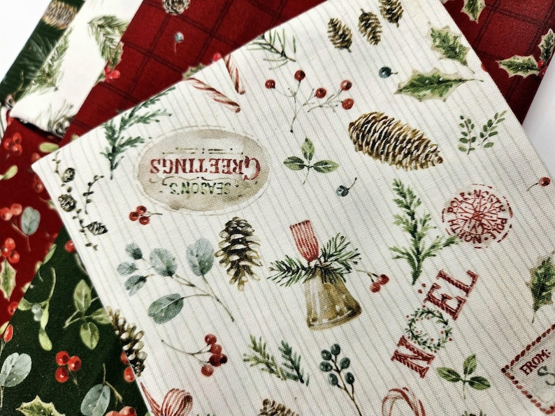 Pode incluir: Um tecido de cor creme com uma estampa natalina de pinhas, folhas de azevinho, bagas vermelhas, sinos e bengalas doces. O texto diz Season's Greetings, Noel e North Pole. Camadas adicionais de tecido em vermelho e verde escuro s&atilde;o vis&iacute;veis.