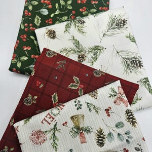 Pode incluir: Quatro quadrados de tecido dobrados com padr&otilde;es festivos. Um &eacute; verde-escuro com bagas vermelhas, um branco com ramos de pinheiro e pinhas, um vermelho-escuro com padr&atilde;o xadrez e azevinho, e um creme com sinos e texto.