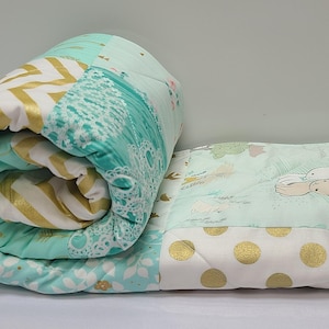 May include: A patchwork quilt with a green, white, and gold color scheme. The quilt features a variety of patterns, including a chevron pattern, a lace pattern, and a polka dot pattern. The quilt also features a design of two bunnies.