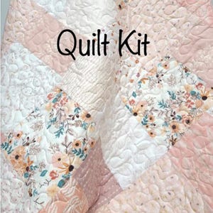 May include: A patchwork quilt kit featuring a floral design in shades of pink, white, and peach. The quilt has a quilted texture and the words "Quilt Kit" are printed on the quilt.
