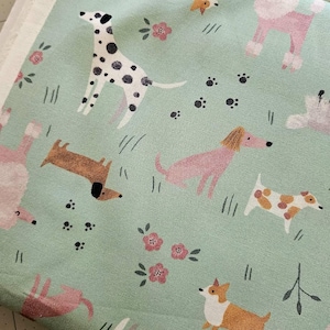 May include: A light green fabric featuring a repeating pattern of various dog breeds, including Dalmatians, Dachshunds, and Poodles. The design also includes pink flowers, paw prints, and blades of grass. The fabric is suitable for sewing projects.