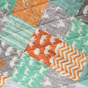 May include: A patchwork quilt with a variety of animal prints, including deer, bears, and foxes. The quilt is made in a mix of orange, green, and gray fabrics.