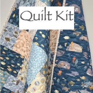 May include: A quilted blanket with a marine life pattern. The quilt features various sea creatures like whales, fish, and turtles in shades of blue, beige, and white. The text "Quilt Kit" is displayed on the front.