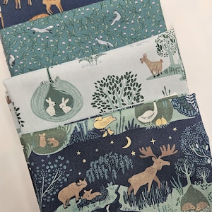 Pode incluir: Uma pilha de quatro peças de tecido dobradas com várias estampas de temática natural. Os padrões incluem veados castanhos sobre azul-marinho, raposas brancas sobre verde-azulado, coelhos brancos em ninhos verdes e uma cena noturna.