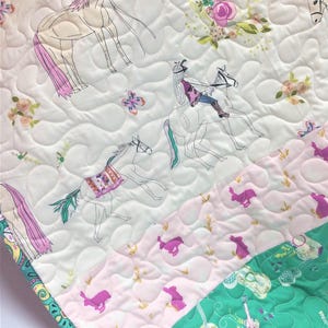May include: Quilted fabric featuring a horse-themed design. The white background is adorned with line drawings of horses, riders, and floral accents. Sections of pink and green fabric with horse and guitar patterns add color.