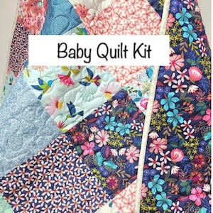 May include: A baby quilt kit featuring a patchwork design with floral and hummingbird patterns in shades of blue, pink, and white. The quilt is trimmed with a white binding.
