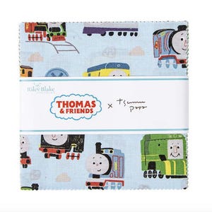 May include: A stack of fabric squares featuring a light blue background with colorful illustrations of Thomas the Tank Engine and his friends. The fabric is wrapped with a white band that reads "Thomas & Friends" and "Riley Blake Designs."