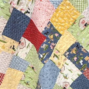 May include: A patchwork quilt featuring a variety of fabric squares with farm-themed prints including barns, animals, and gingham patterns in shades of blue, green, yellow, red, and white, all joined with a continuous wavy machine quilting stitch.