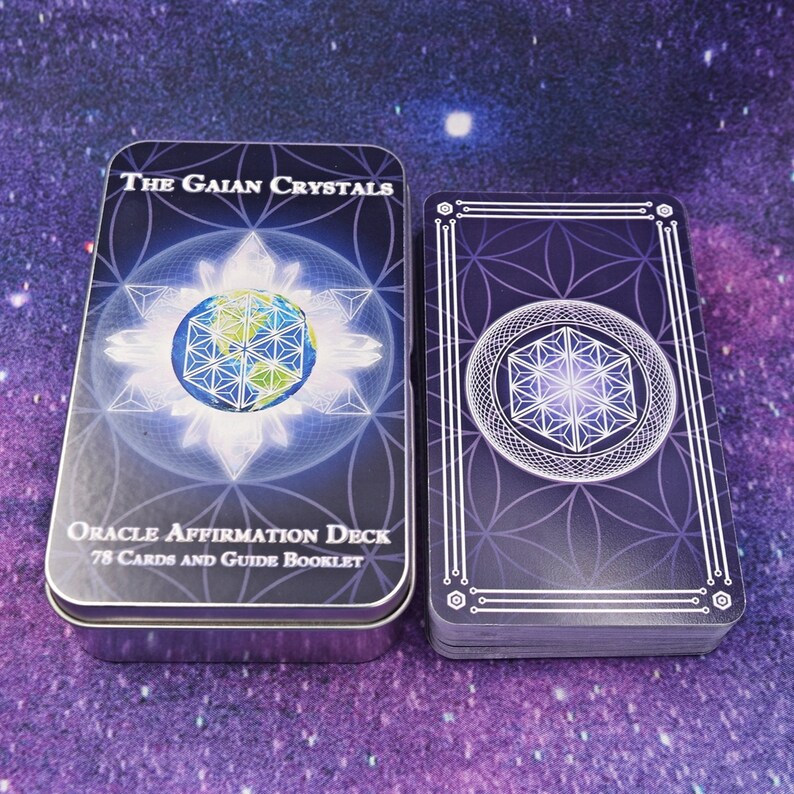 Może przedstawiać: Srebrne pudełko z blachy z fioletowym i białym wzorem przedstawiającym glob otoczony kryształami. Tekst na pudełku brzmi "The Gaian Crystals Oracle Affirmation Deck 78 Cards and Guide Booklet".