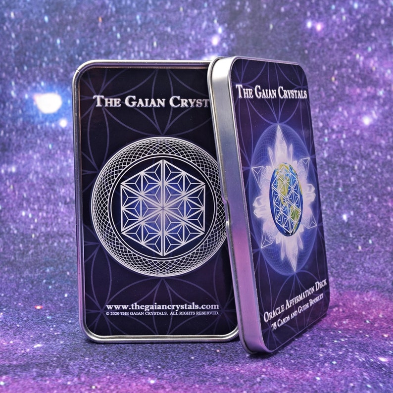 Może przedstawiać: Dwa srebrne pudełka z czarnymi i niebieskimi wzorami. Pudełko po lewej stronie ma wz&oacute;r geometryczny i tekst "THE GAIAN CRYSTALS" oraz "www.thegaiancrystals.com". Pudełko po prawej stronie ma globus z geometrycznym wzorem i tekst "THE GAIAN CRYSTALS" oraz "ORACLE AFFIRMATION DECK 78 CARDS AND GUIDE BOOKLET".