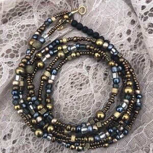 May include: A multi-strand beaded wrap bracelet with gold, bronze, silver, and black beads. The bracelet is wrapped around itself and has a gold-colored clasp. The beads are various shapes and sizes.