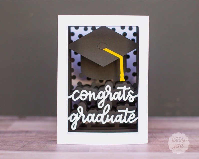 Puede incluir: Una tarjeta blanca con un fondo de lunares blanco y negro. Un gorro de graduaci&oacute;n negro con un borla amarilla est&aacute; en el centro de la tarjeta. Las palabras "congrats graduate" est&aacute;n escritas en blanco en la tarjeta.