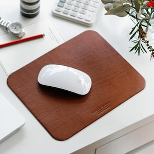 Könnte beinhalten: Ein braunes Leder-Mauspad mit einer weißen kabellosen Maus darauf. Das Mauspad trägt den Text "Franklin & Maxwell".