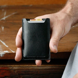 May include: A black leather card holder with a small pocket for cash. The card holder has the text "WATERFIELD DESIGNS" embossed on the bottom.