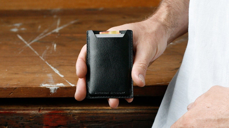 May include: A black leather card holder with a small pocket for cash. The card holder has the text "WATERFIELD DESIGNS" embossed on the bottom.