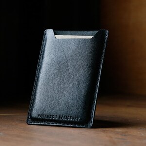 May include: A black leather card holder with the text "Patterson  Brandery" embossed on the front.