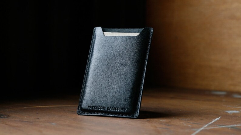 May include: A black leather card holder with the text "Patterson  Brandery" embossed on the front.