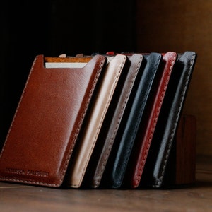 May include: A set of eight leather card holders in various colors, including brown, tan, gray, black, and red. The holders are stacked on top of each other and have a stitched edge.