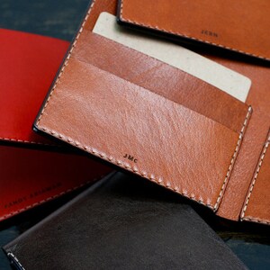 May include: A close-up of four leather wallets in different colors, including red, brown, and black. The wallets have multiple card slots and a billfold. The wallets are made of high-quality leather and have a stitched edge.