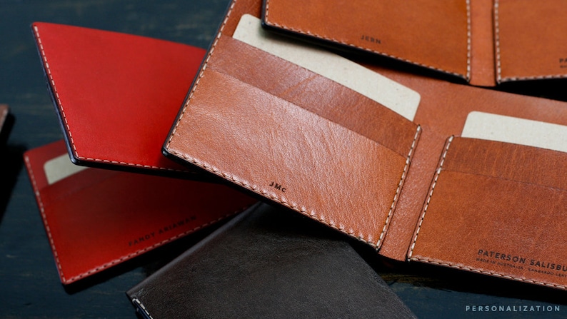 May include: A close-up of four leather wallets in different colors, including red, brown, and black. The wallets have multiple card slots and a billfold. The wallets are made of high-quality leather and have a stitched edge.