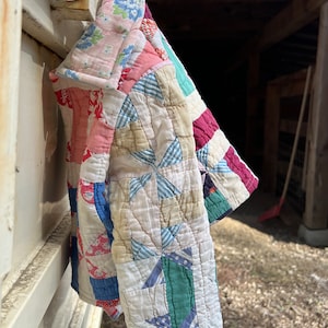 May include: A colorful patchwork quilt with a variety of floral and geometric patterns in shades of pink, blue, green, and white. The quilt is hanging on a hook.