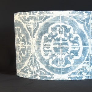 May include: Cylindrical lampshade featuring a repeating pattern of blue and white floral tile designs. The lampshade is made of a rigid material and has a distressed, aged appearance. The design is reminiscent of traditional Portuguese or Spanish tiles.