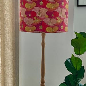K&ouml;nnte beinhalten: Eine Stehlampe aus Holz mit floralem Lampenschirm. Der Lampenschirm hat ein Muster aus roten, rosa, gelben und wei&szlig;en Blumen. Der Holzfu&szlig; der Lampe ist hellbraun.
