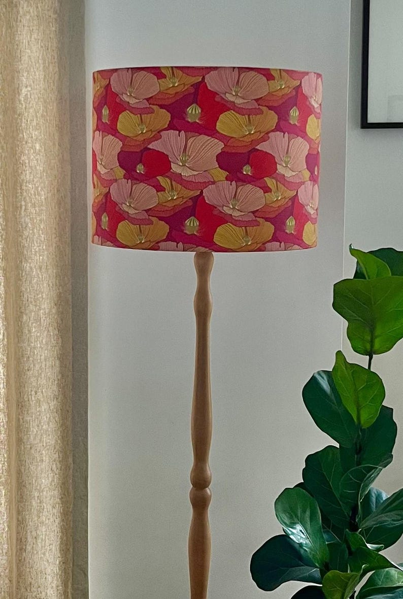 K&ouml;nnte beinhalten: Eine Stehlampe aus Holz mit floralem Lampenschirm. Der Lampenschirm hat ein Muster aus roten, rosa, gelben und wei&szlig;en Blumen. Der Holzfu&szlig; der Lampe ist hellbraun.