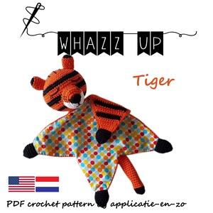 Può includere: Un peluche di tigre all'uncinetto con una coperta a pois. La tigre è arancione e nera con un viso bianco. La coperta è blu, gialla, arancione e rossa. Il testo "Whazz Up Tiger" è sopra il peluche.