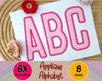 May include: A white felt applique with the letters "ABC" in light pink, outlined with a darker pink stitched border. The words "Applique Alphabet" are below the letters. The image also includes two crocheted flower embellishments.