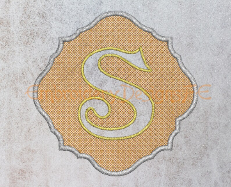 May include: A yellow embroidered letter "S" in a decorative, scalloped frame. The frame is a light gray color and the background is a light orange.