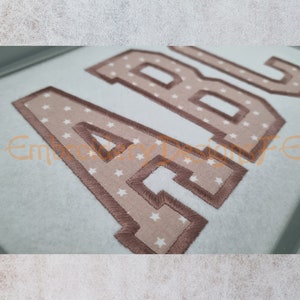 May include: Embroidered letters A, B, and C in a brown color with a white star pattern on a light blue fabric.